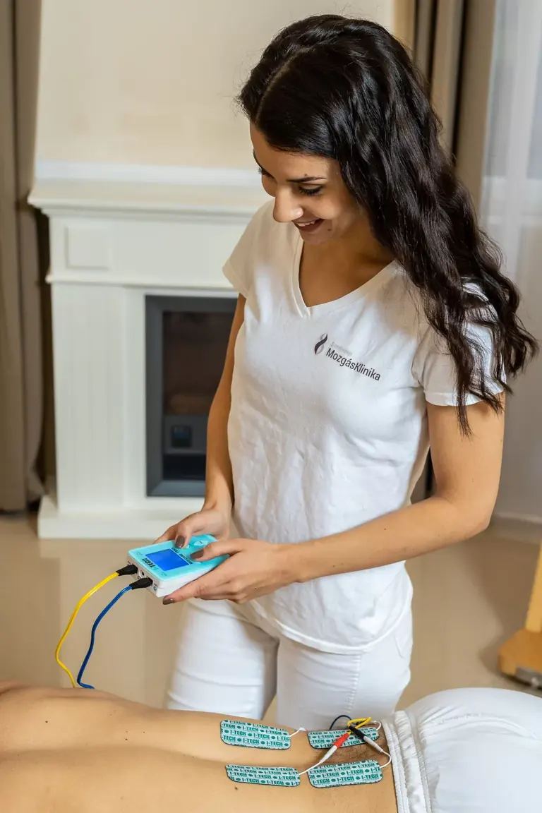 Gyógytornász elektroterápiás készüléket állít be egy fekvő páciens mellett